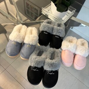 Könnte beinhalten: Sechs Paar personalisierte Hausschuhe mit Kunstfellbesatz. Die Hausschuhe sind in Grau, Schwarz und Rosa. Die Namen "Nana", "ES", "Tasha" und "Danny" sind auf die Hausschuhe gestickt.