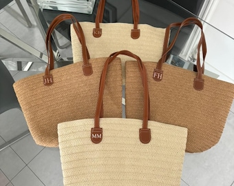 May include: Four straw tote bags with brown leather handles and personalized initials. The bags are in various shades of brown and beige.