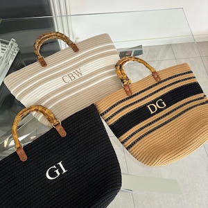 May include: Three woven tote bags with bamboo handles. The bags are striped in beige and black, white and beige, and black. Each bag has a white monogram on the front: CBW, DG, and GI.