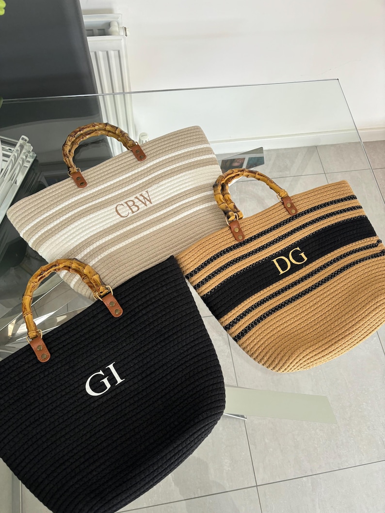 May include: Three woven tote bags with bamboo handles. The bags are striped in beige and black, white and beige, and black. Each bag has a white monogram on the front: CBW, DG, and GI.
