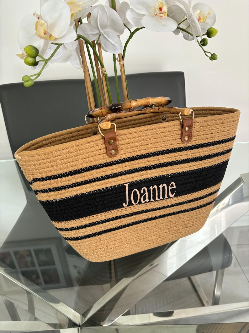 May include: A tan and black striped tote bag with bamboo handles. The bag has the name "Joanne" embroidered on the front.