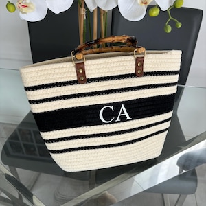 May include: A white and black striped tote bag with a bamboo handle and the initials "CA" embroidered on the front.