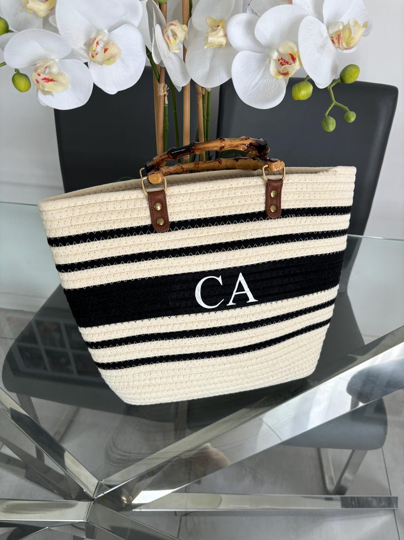 May include: A white and black striped tote bag with a bamboo handle and the initials "CA" embroidered on the front.