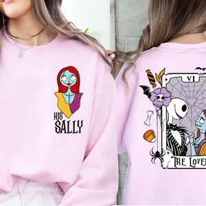 two pink sweatshirts with different designs. The left sweatshirt features a cartoon character, while the right sweatshirt has a tarot card design with a skeleton and a pumpkin.