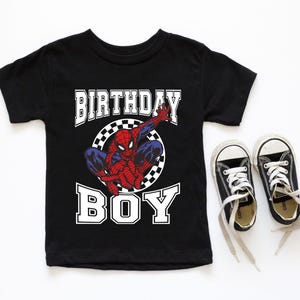 A black t-shirt with a Spider-Man graphic and the text "BIRTHDAY BOY" printed on it, along with a pair of black and white sneakers.