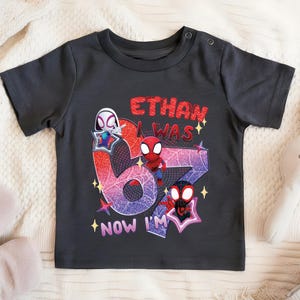A black t-shirt with a graphic design featuring Spider-Man characters and the text "ETHAN WAS 6 NOW I'M" printed on it.