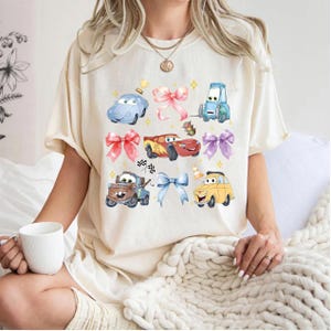 A woman wearing a white t-shirt with a graphic of cartoon cars and various other objects, including a cup and a blanket.