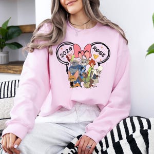 K&ouml;nnte beinhalten: Hellrosa Sweatshirt mit einem Cartoon-Motiv von Filmfiguren, mit den Texten "2020" und "Rose" in einem Mickey Mouse Ohren-Design. Das Sweatshirt hat eine einfarbige, hellrosa Farbe.