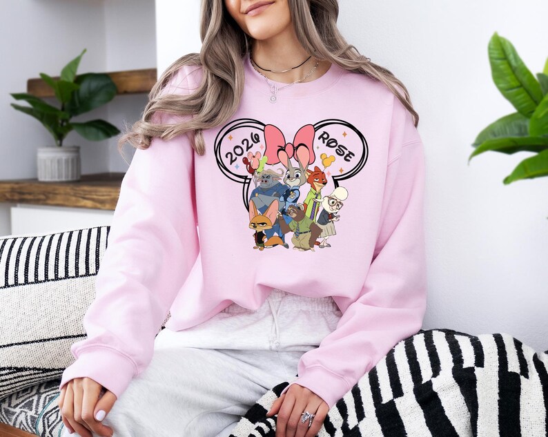 K&ouml;nnte beinhalten: Hellrosa Sweatshirt mit einem Cartoon-Motiv von Filmfiguren, mit den Texten "2020" und "Rose" in einem Mickey Mouse Ohren-Design. Das Sweatshirt hat eine einfarbige, hellrosa Farbe.