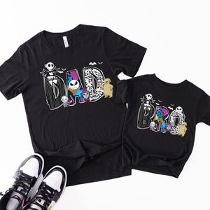 A black t-shirt with a Halloween-themed design and a smaller t-shirt underneath it, along with a pair of sneakers.