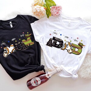 two t-shirts with the same design, one black and one white, along with a bottle of wine and some flowers.