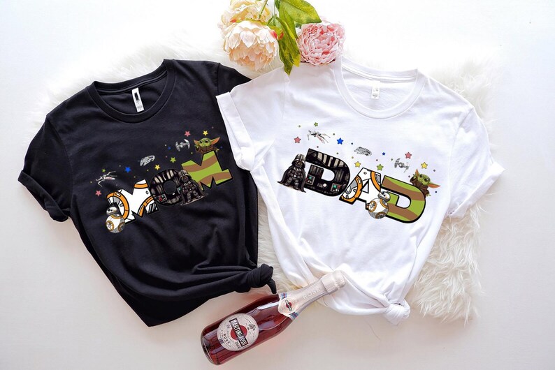 two t-shirts with the same design, one black and one white, along with a bottle of wine and some flowers.