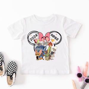 K&ouml;nnte beinhalten: Wei&szlig;es Kurzarm-T-Shirt mit einem Cartoon-Motiv von Zootopia, einer rosa Schleife und dem Text "2020 ROSE". Dazu geh&ouml;ren schwarz-wei&szlig; karierte Slip-on-Schuhe.
