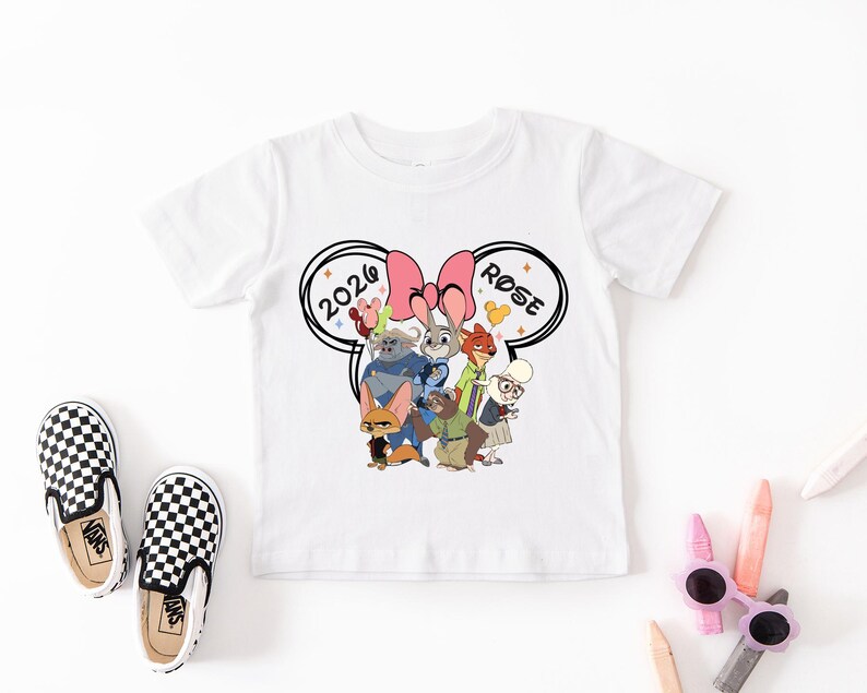 K&ouml;nnte beinhalten: Wei&szlig;es Kurzarm-T-Shirt mit einem Cartoon-Motiv von Zootopia, einer rosa Schleife und dem Text "2020 ROSE". Dazu geh&ouml;ren schwarz-wei&szlig; karierte Slip-on-Schuhe.