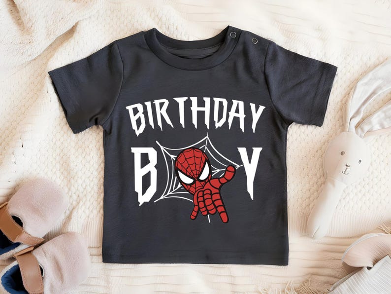 A black t-shirt with a Spiderman graphic and the text "BIRTHDAY B" printed on it, along with a pair of sandals and a stuffed rabbit.