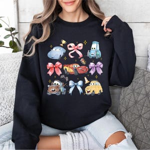 A woman wearing a black sweatshirt with a graphic design featuring various cartoon cars and characters from the Cars movie franchise.