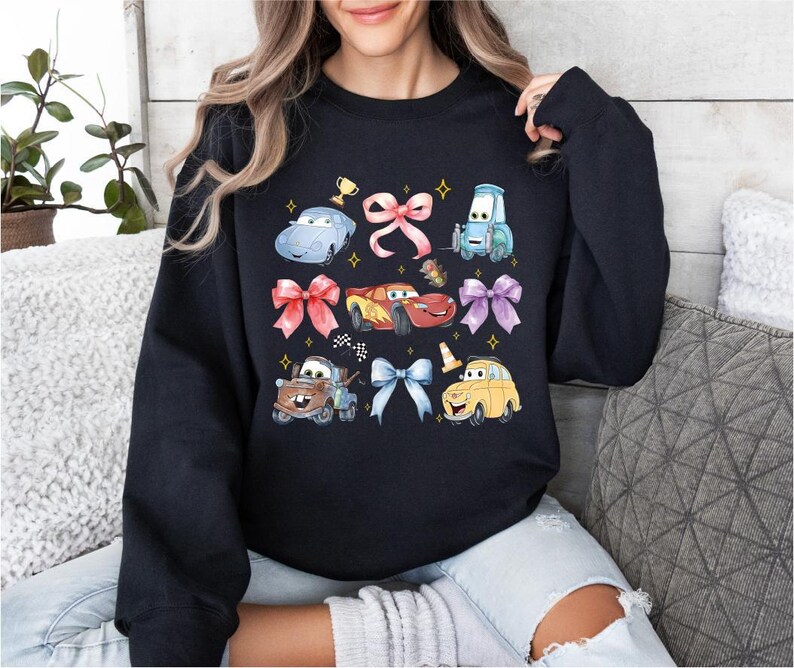 A woman wearing a black sweatshirt with a graphic design featuring various cartoon cars and characters from the Cars movie franchise.
