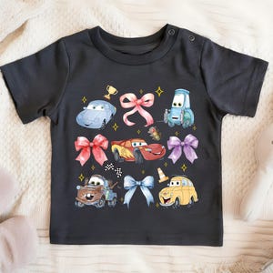 A black t-shirt with a colorful graphic design featuring cartoon cars and other characters, along with bows and stars.