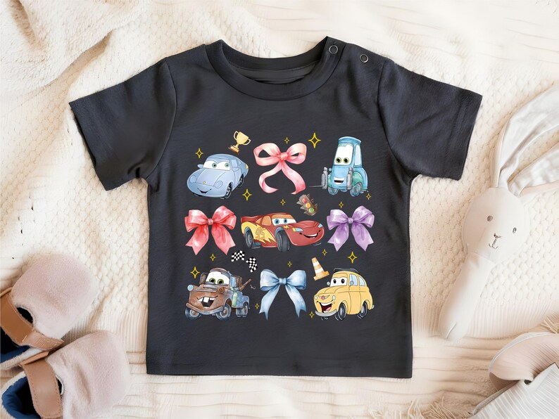 A black t-shirt with a colorful graphic design featuring cartoon cars and other characters, along with bows and stars.