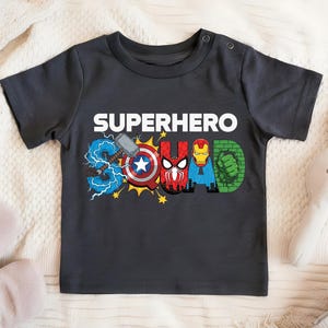 A black t-shirt with the text "SUPERHERO SQUAD" printed on it, featuring various superhero logos and symbols.