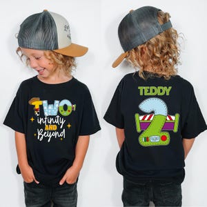 A young boy wearing a black t-shirt with a cartoon character and text, and a baseball cap, smiling at the camera.