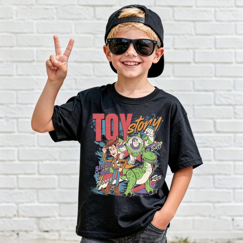 A young boy wearing a black t-shirt with a graphic of Woody and Buzz from Toy Story, smiling and making a peace sign gesture.