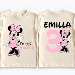 two white t-shirts with a Minnie Mouse design and text. The text on the t-shirts reads "I'm this MINNIE" and "EMILLA 3".