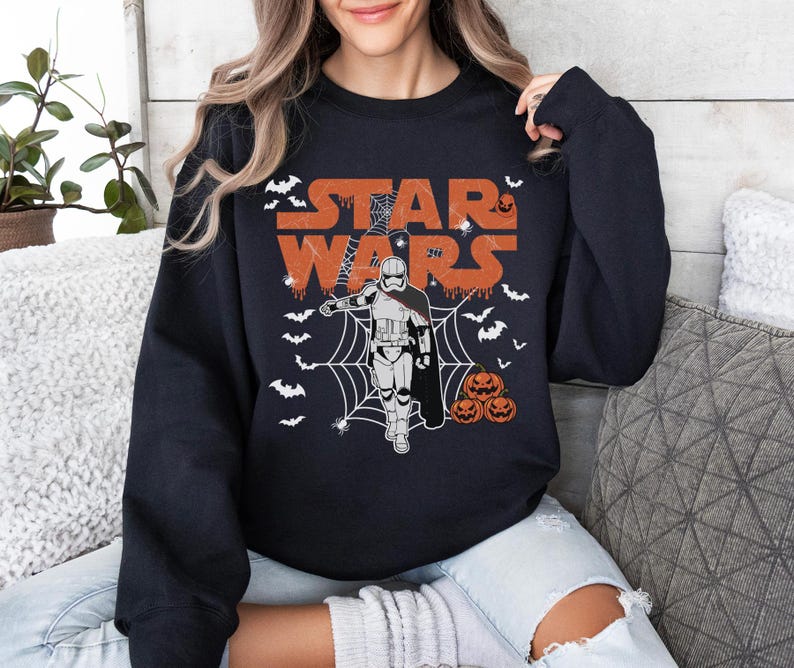 A woman wearing a black sweatshirt with a Star Wars-themed graphic design, including a stormtrooper, spider web, and Halloween pumpkins.