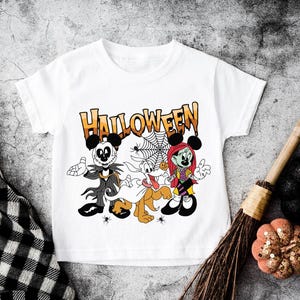 A white t-shirt with a Halloween-themed graphic design featuring characters from the Disney movie " jack Skellington and Sally" and a spider web.