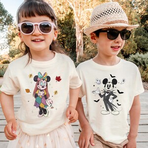 Two children wearing Mickey Mouse-themed t-shirts stand together in a park.