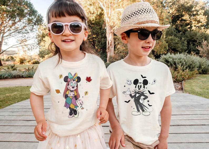 Two children wearing Mickey Mouse-themed t-shirts stand together in a park.