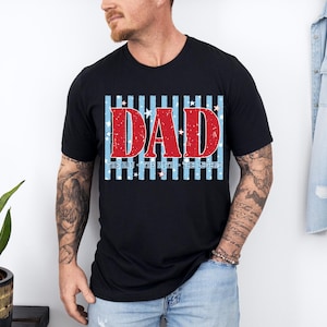 May include: Black t-shirt with a patriotic design. The word "DAD" is in red, with white stars, over blue and white stripes. The text "THE MAN - THE MYTH - THE LEGEND" is below the word "DAD".