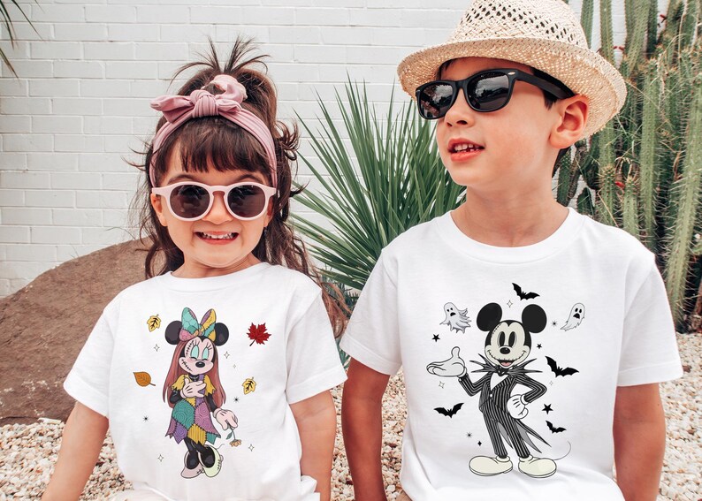 A young girl and a young boy are standing together, both wearing white t-shirts with cartoon characters and designs.