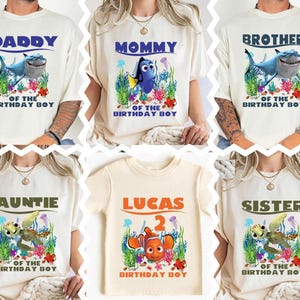 May include: Cream-colored t-shirts with various "Finding Nemo" character graphics and text. Designs include "Daddy," "Mommy," "Brother," "Auntie," "Lucas 2," and "Sister," with "Of The Birthday Boy" text. The shirts feature colorful underwater scenes.