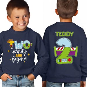 A young boy wearing a navy blue sweatshirt with a cartoon character and text printed on it.