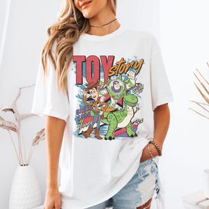 A woman wearing a white t-shirt with a colorful graphic of characters from the Toy Story movie.