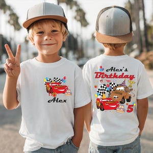 A young boy wearing a white t-shirt with a personalized Cars-themed birthday design and text on the back.