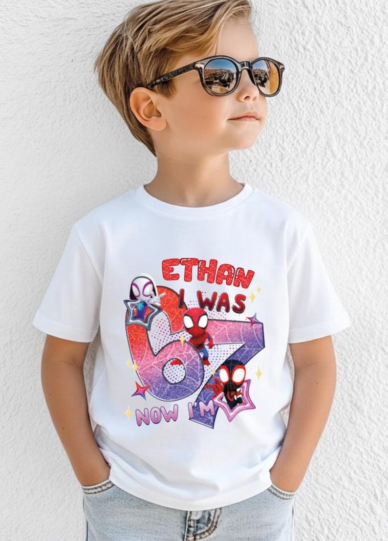 A young boy wearing a white t-shirt with a graphic design featuring Spider-Man characters and text.