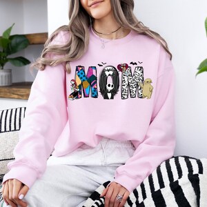 A woman wearing a pink sweatshirt with the word "MOM" printed on it, sitting on a couch with a striped pillow.