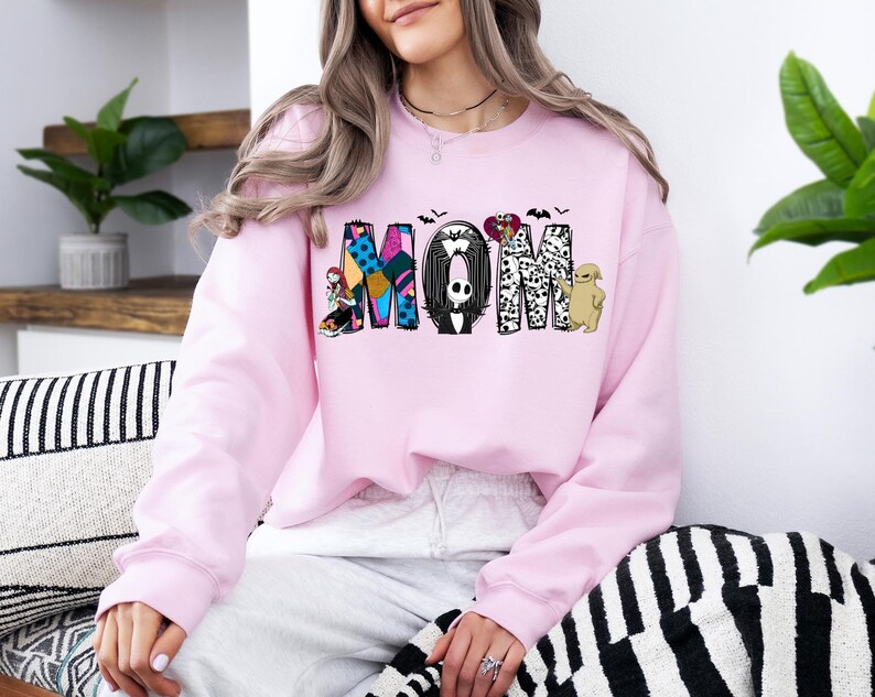 A woman wearing a pink sweatshirt with the word "MOM" printed on it, sitting on a couch with a striped pillow.