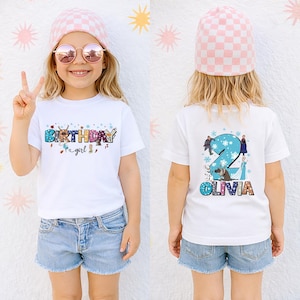 A young girl wearing a white t-shirt with a birthday message and a pink beanie is smiling and making a peace sign.