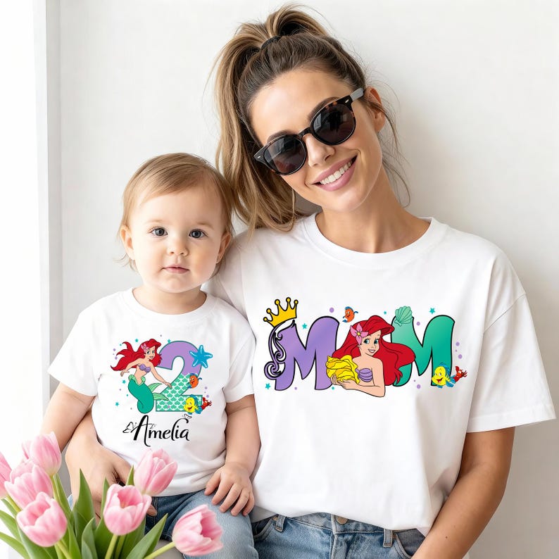 A woman and a young child wearing matching white t-shirts with the name "Amelia" printed on them, smiling and posing together.