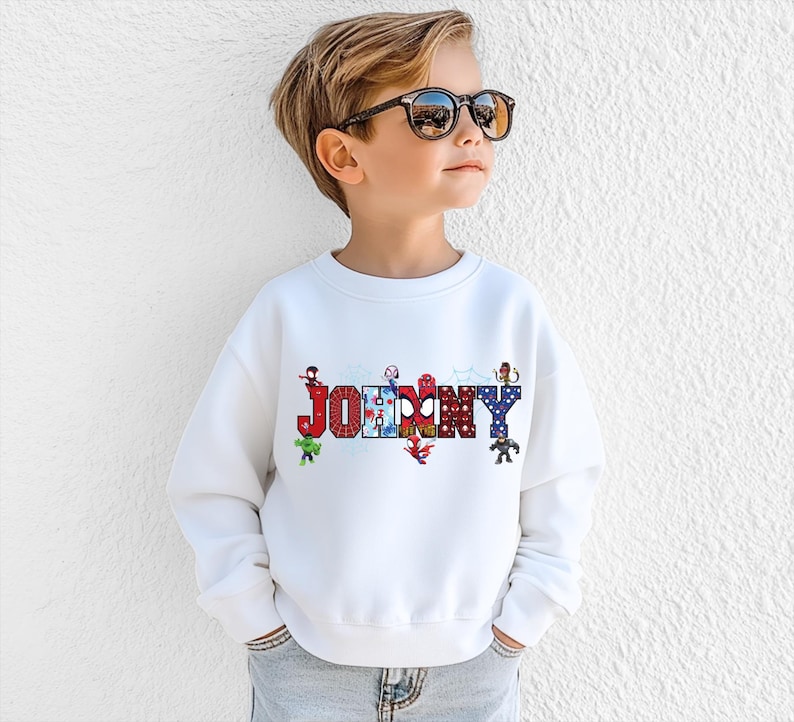 A young boy wearing a white sweatshirt with the word "JOMMY" printed on it, standing against a white wall.