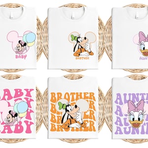 six white t-shirts with Disney character designs, including Minnie Mouse, Goofy, and Daisy Duck. The t-shirts feature various Disney character names and phrases, such as "BABY", "BROTHER", "AUNTIE", "BABY", "BROTHER", and "AUNTIE".