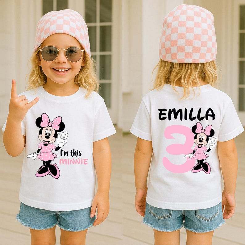 A young girl wearing a white t-shirt with a Minnie Mouse design and the text "I'm this Minnie" printed on it, smiling and making a hand gesture.