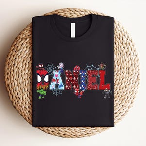 A black t-shirt with a colorful graphic design featuring the letters of the word "DAMNEL" surrounded by various Spider-Man characters.