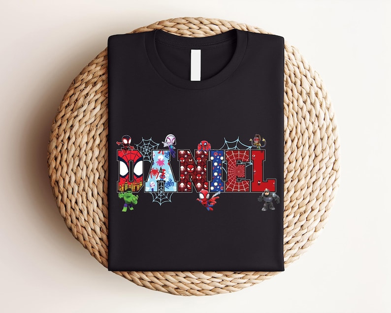 A black t-shirt with a colorful graphic design featuring the letters of the word "DAMNEL" surrounded by various Spider-Man characters.