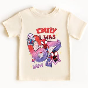 A white t-shirt with a graphic design featuring a Spider-Man character and text that says "Emilly was 67 now I'm".