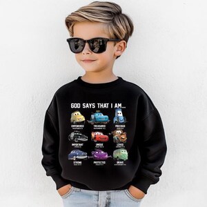 A young boy wearing a black sweatshirt with a graphic of various cars and the text "God says that I am" printed on it.