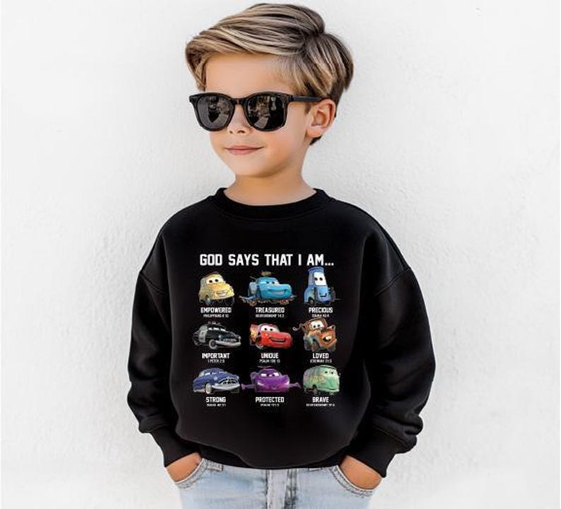A young boy wearing a black sweatshirt with a graphic of various cars and the text "God says that I am" printed on it.